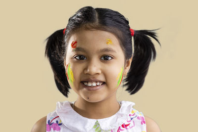 Portrait of a cute indian girl child with colorful cheek on yellow background