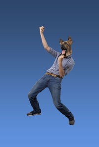 Low angle view of young man jumping against clear blue sky