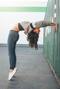 Full length of female athlete stretching on street by cargo container