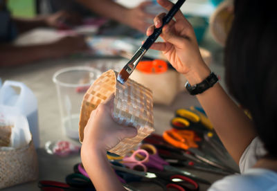 Cropped hands of woman painting wicker basket at table