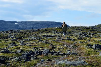 Rear view of man standing on rock against sky