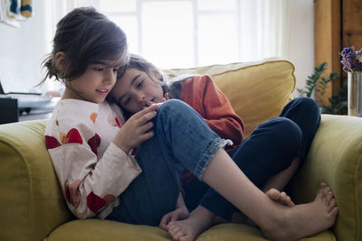 Girl using smart phone sitting with sister on armchair in living room at home