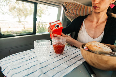 Midsection of woman holding drink while sitting on table