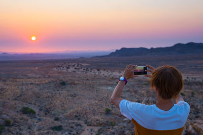 Rear view of woman photographing at sunset