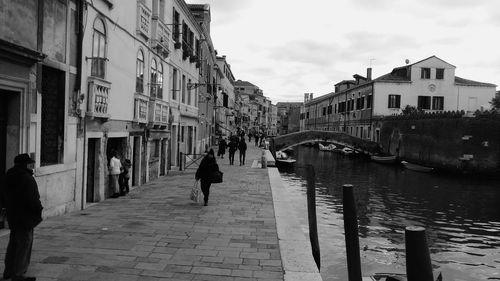 People walking on sidewalk in city against sky