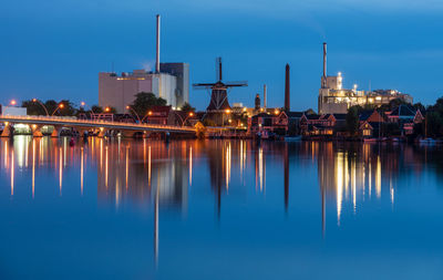 Illuminated buildings by river against sky at dusk