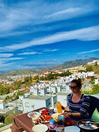 Full length of woman sitting at restaurant against cityscape