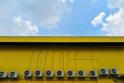 Low angle view of air conditioners on yellow building against sky