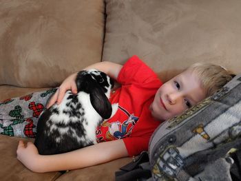 Boy and rabbit lying on sofa at home