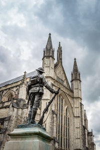 Low angle view of statue by winchester cathedral against cloudy sky