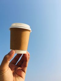 Low angle view of person holding drink against clear sky