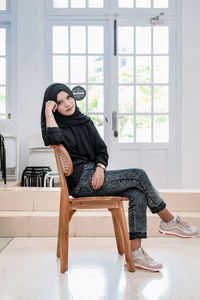 Portrait of young woman sitting on chair at home