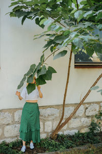 Woman standing by plant against wall