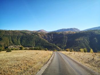 Road leading towards mountains against clear blue sky