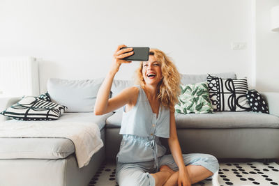 Young woman using mobile phone while sitting on bed at home