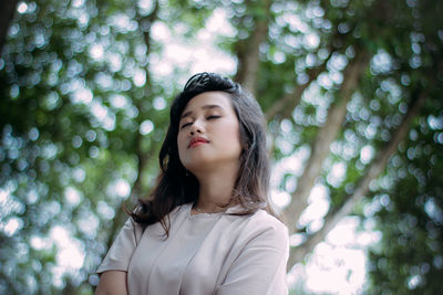 Low angle view of young woman standing against trees