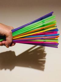 Close-up of hand holding colored pencils on table against wall