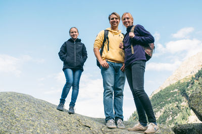 Full length portrait of friends standing on rock against sky