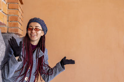 Smiling woman gesturing against wall