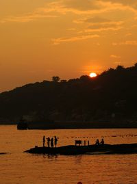 Silhouette people on shore against sky during sunset