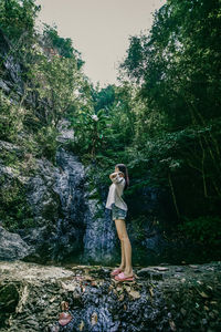 Full length of woman standing on rock in forest