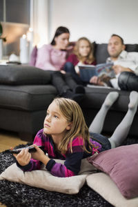 Girl watching tv on floor with family in background