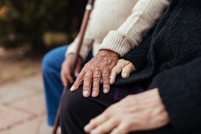 Crop of anonymous elderly couple holding hands while sitting on a park bench