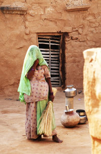 Woman wearing sari holding broom while standing in yard at village