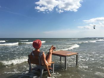 Rear view of woman sitting on chair at beach against sky