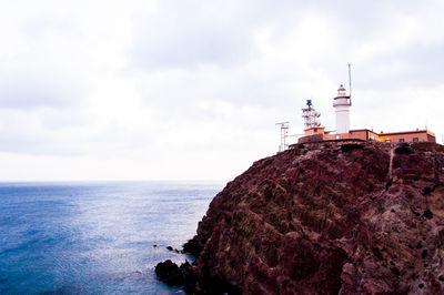 Lighthouse on cliff by sea against sky