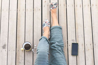 Low section of woman with coffee and smart phone on wooden plank