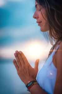 Side view of woman doing yoga while sitting against sky during sunset