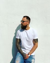 Young man wearing sunglasses standing against wall