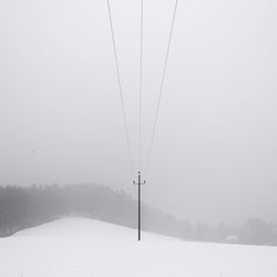 Overhead cable car over snow covered field against sky
