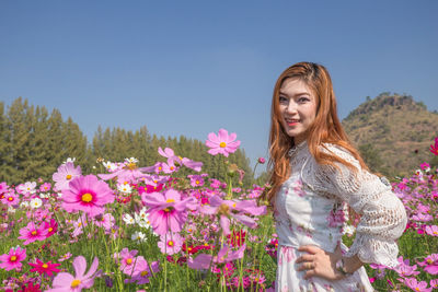 Beautiful young woman standing by flowering plants against clear sky