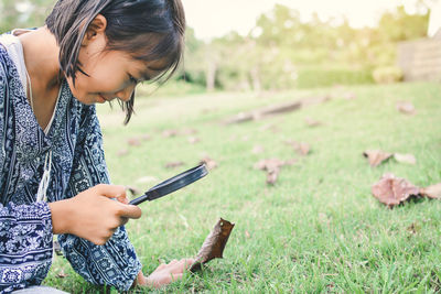 Smiling girl looking through magnifying glass at grassy field