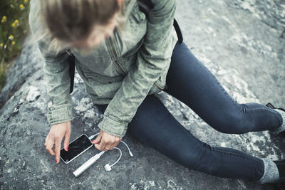 High angle view of woman connecting portable charger to smart phone on rock