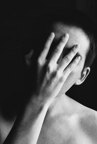 Close-up of shirtless man covering face against black background