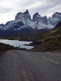 Road leading towards lake by snowcapped mountains against sky