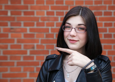 Portrait of smiling young woman against brick wall