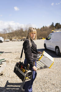 Female electrician carrying ladder and toolbox standing on road