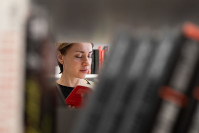 Focused female mature student picking book from bookshelf for educational project preparing for exam