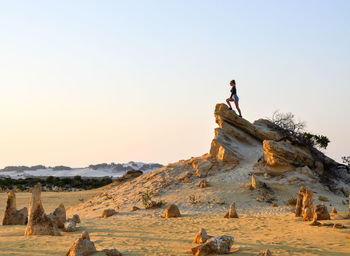 Full length of woman standing on rock formation in desert against clear sky