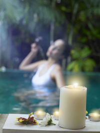 Close-up of lit candle with woman swimming in pool