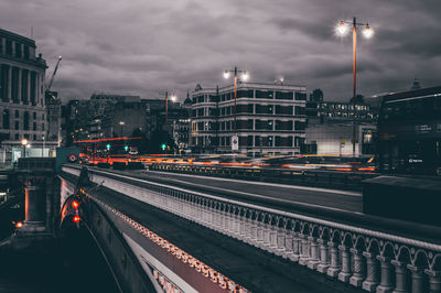 Light trails on railroad tracks in city against sky at night