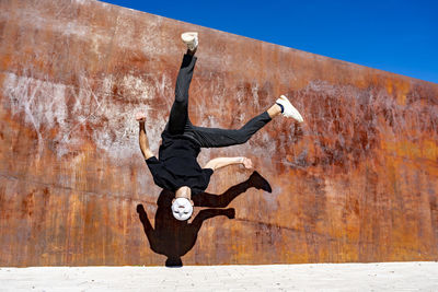 Man wearing whit mask jumping against brown wall during sunny day