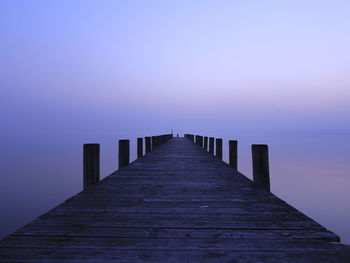 Pier over calm lake against sky during sunset