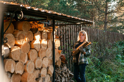 A beautiful blonde woman in a plaid shirt collects wood from a wood-burner. everyday rural life.