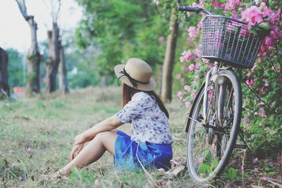 Side view of young woman sitting with bicycle parked at park