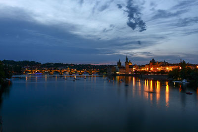 Scenic view of river by illuminated city against sky at dusk